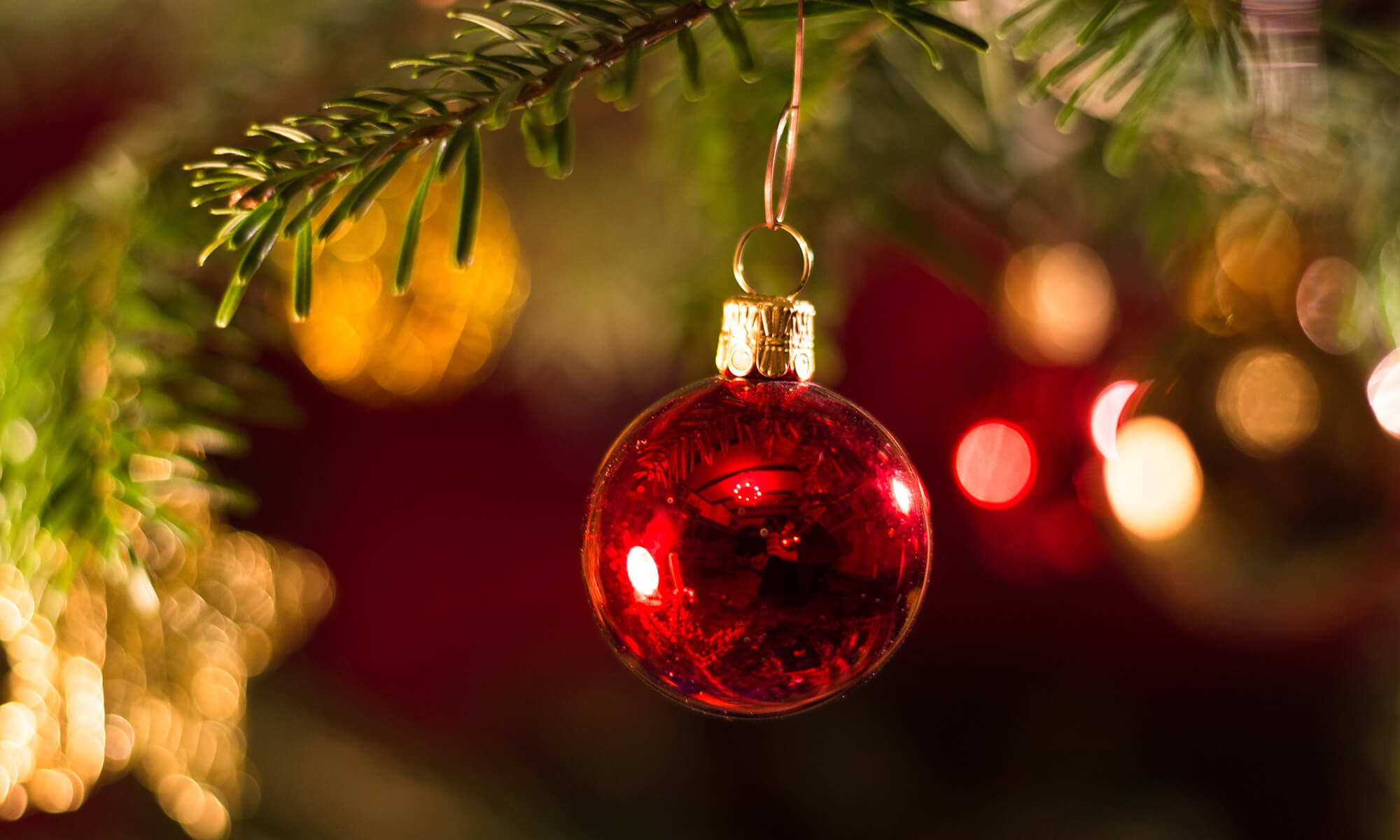 Rode kerstbal aan een kerstboom met Spaanse kerstlampjes op de achtergrond